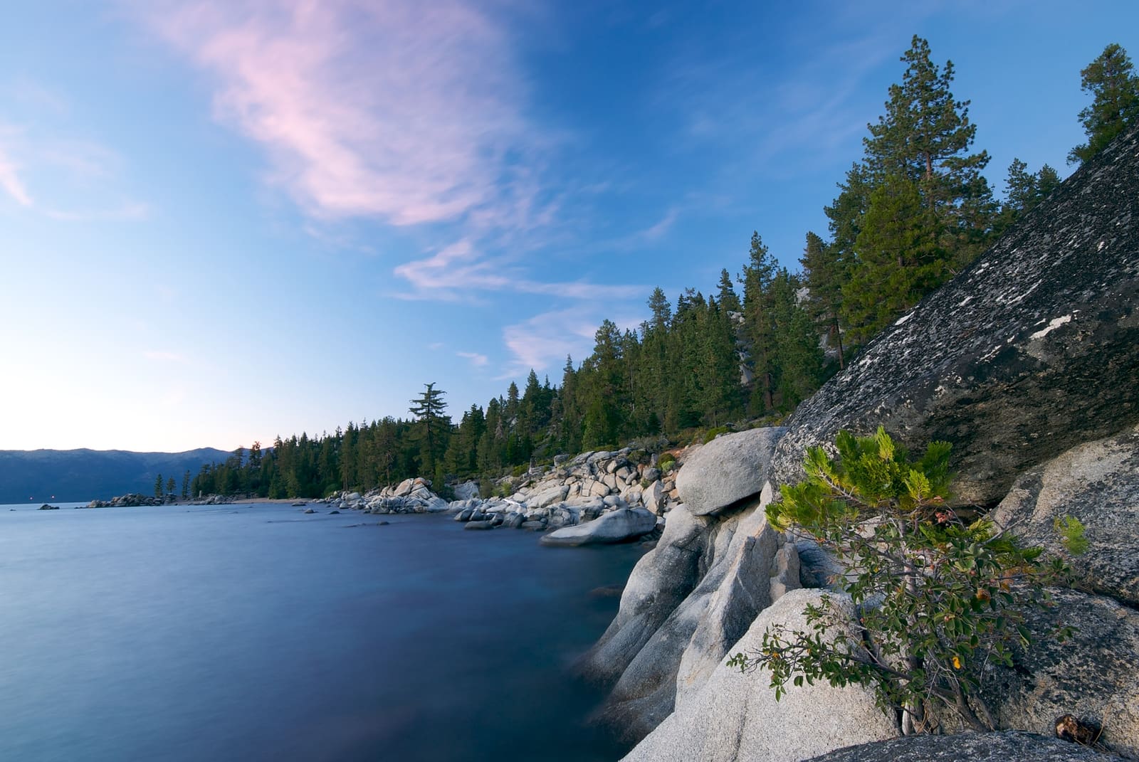 The rock covered coastline of Lake Tahoe at sunset with thick forests