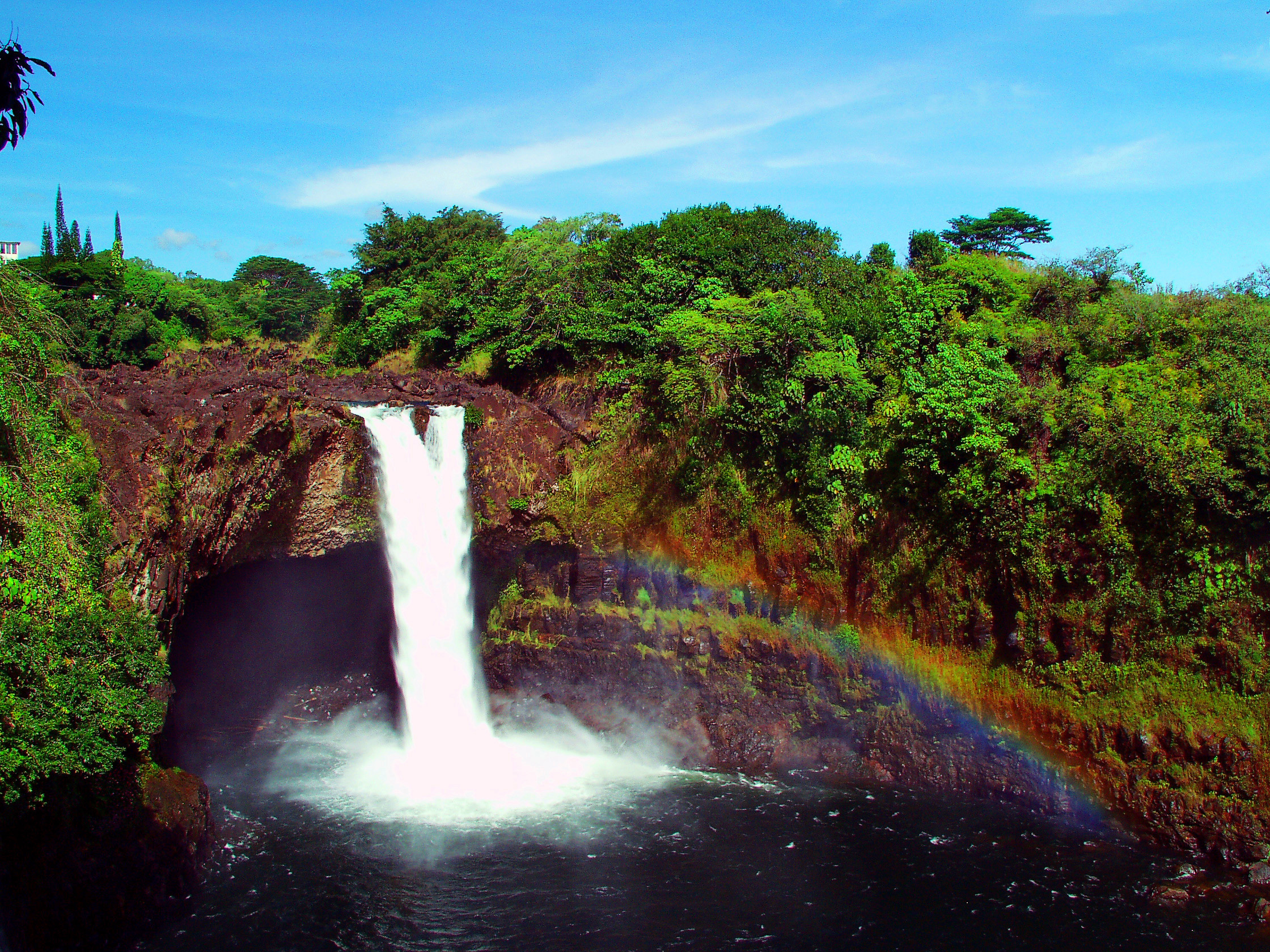 Waterfall with rainbow in Hawaii with water pool at the bottom
