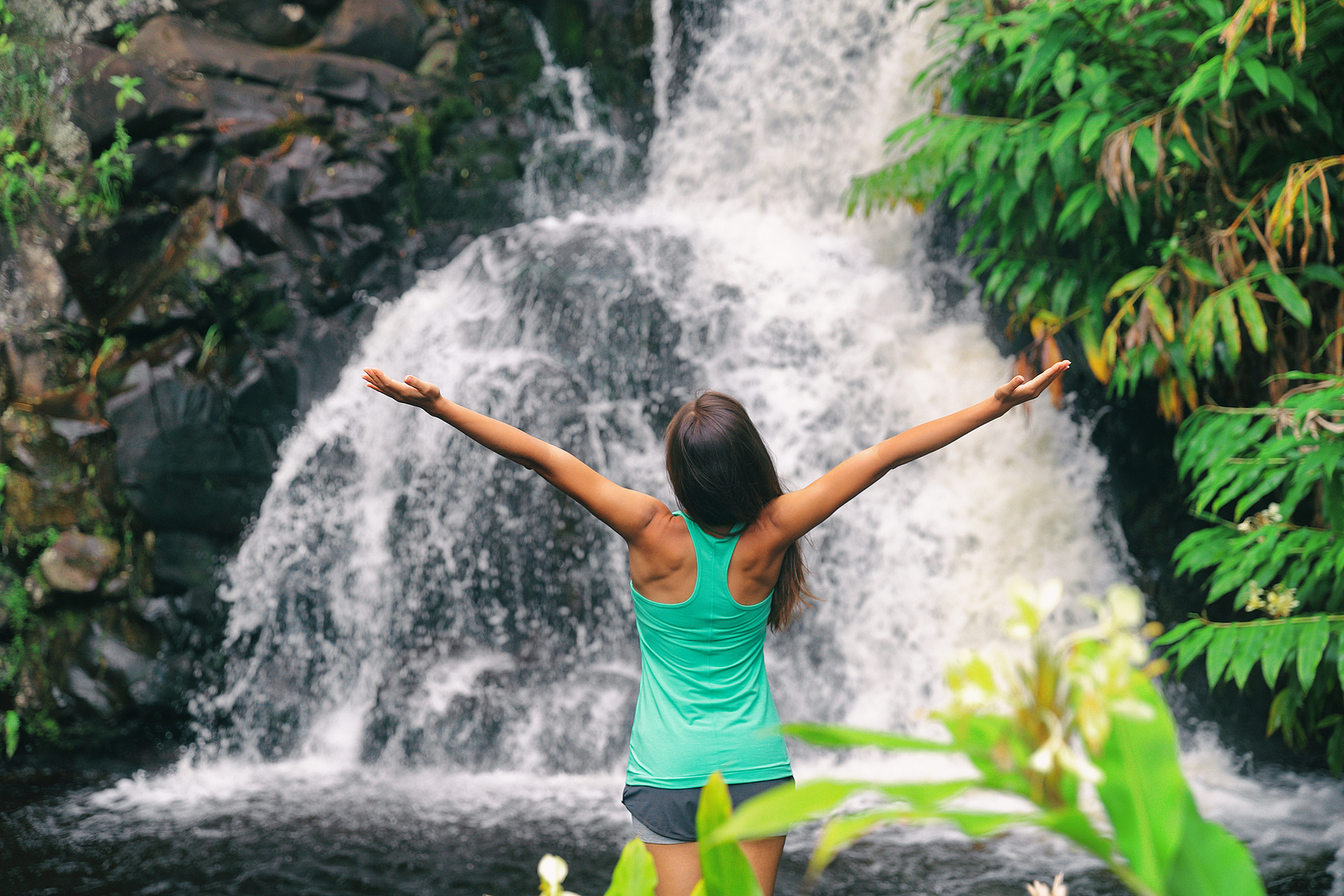 Hawaii travel nature waterfall woman hiker at Canyon Trail Waipoo Falls in Waimea, Kauai island, USA. Freedom happy girl with open arms meditating yoga in rainforest.